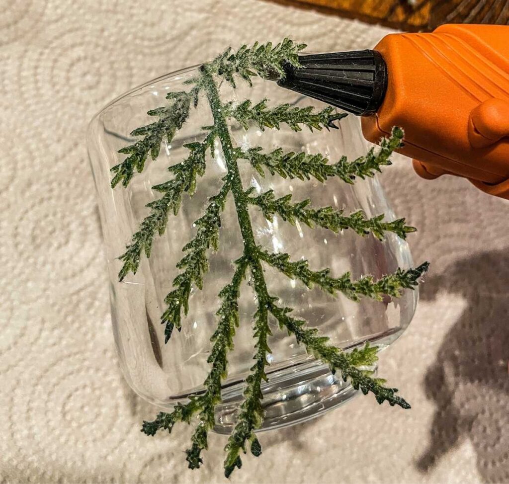 hot glue gun gluing the branches of a faux tree onto a candle holder