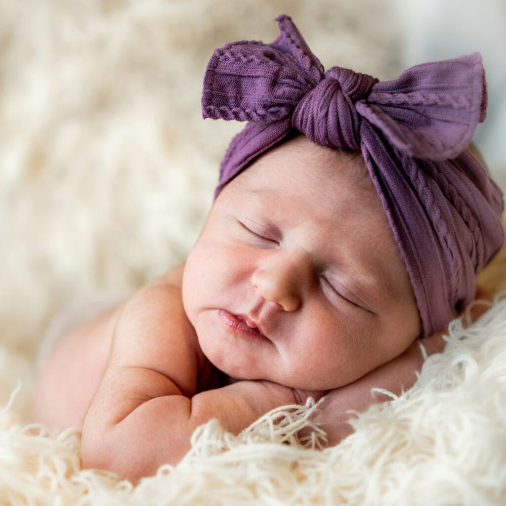 Baby girl asleep with a big purple bow on her head