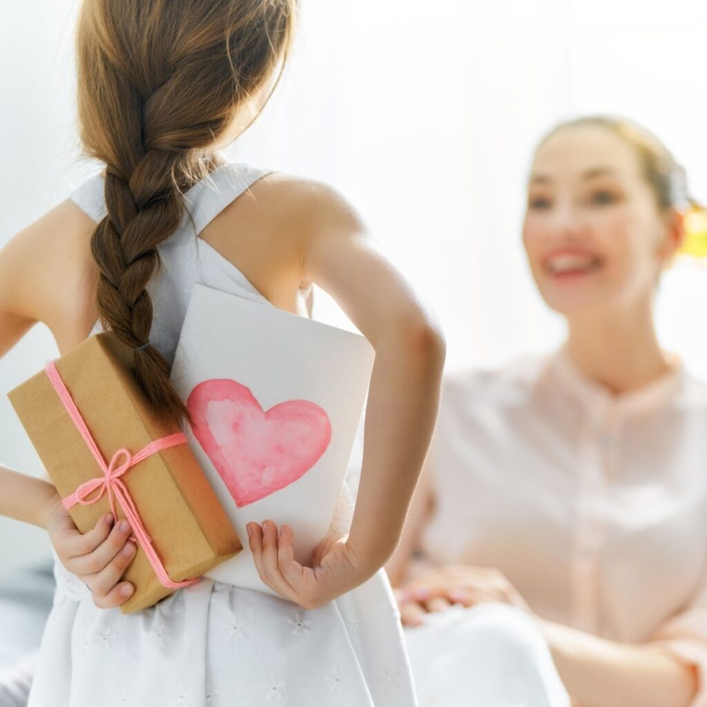 Childing holding a mother's day card and book wrapped as a gift for mom
